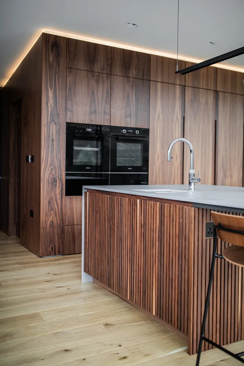 Walnut kitchen with a fluted island and lit tall cabinets
