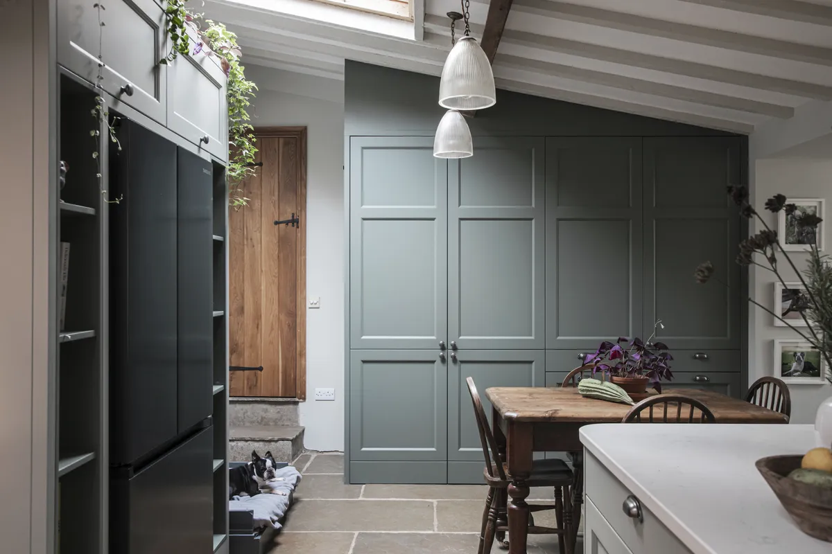 Sage green shaker larder cupboards beside a farmhouse dining table