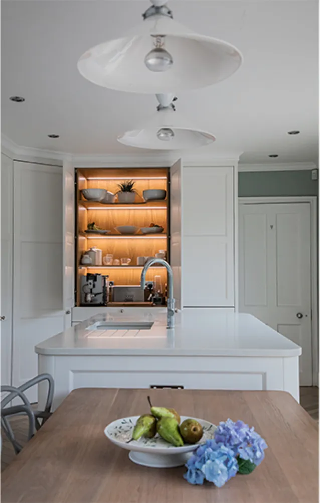 White shaker kitchen with a lit oak-lined pantry cupboard behind the island