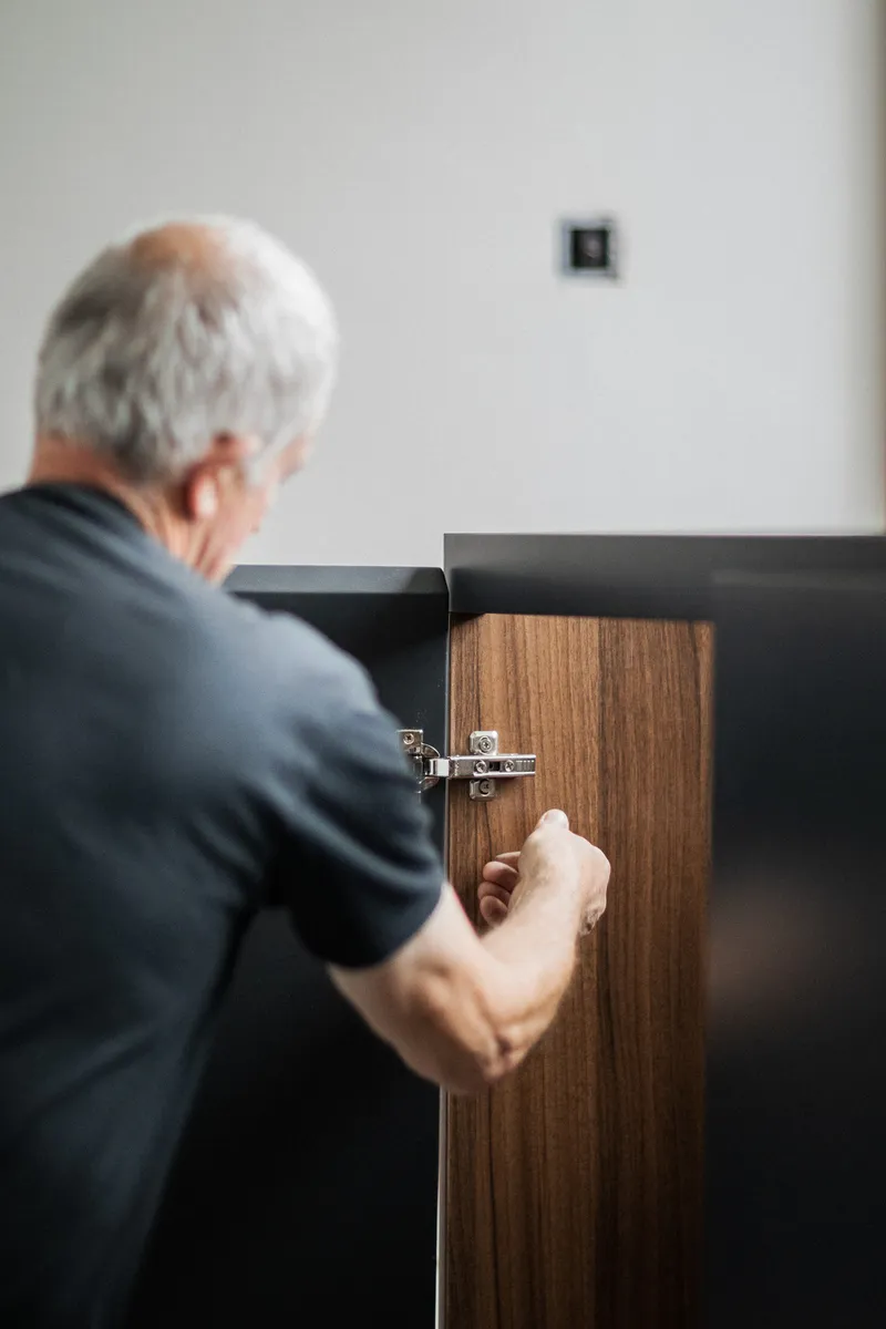 A fitter adjusting the hinge of a walnut cabinet door