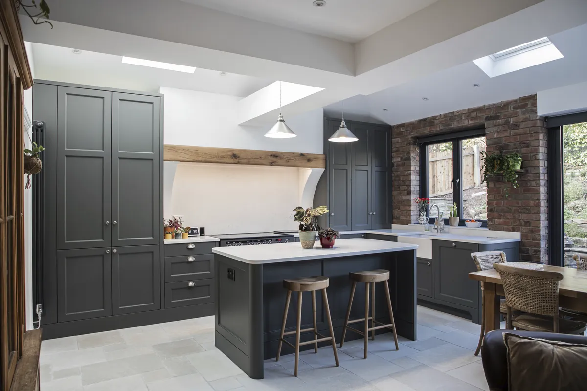 Dark grey shaker kitchen with an oak beam, island and bar stools under skylights